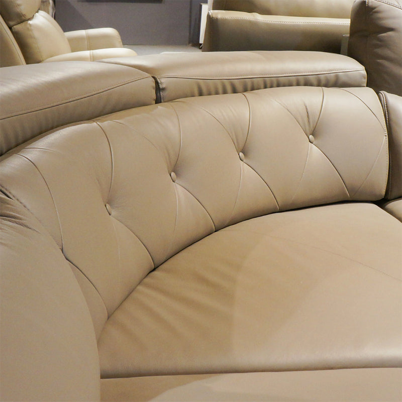 Beige leather sectional sofa with tufted backrests in a room setting.