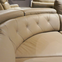 Beige leather sectional sofa with tufted backrests in a room setting.